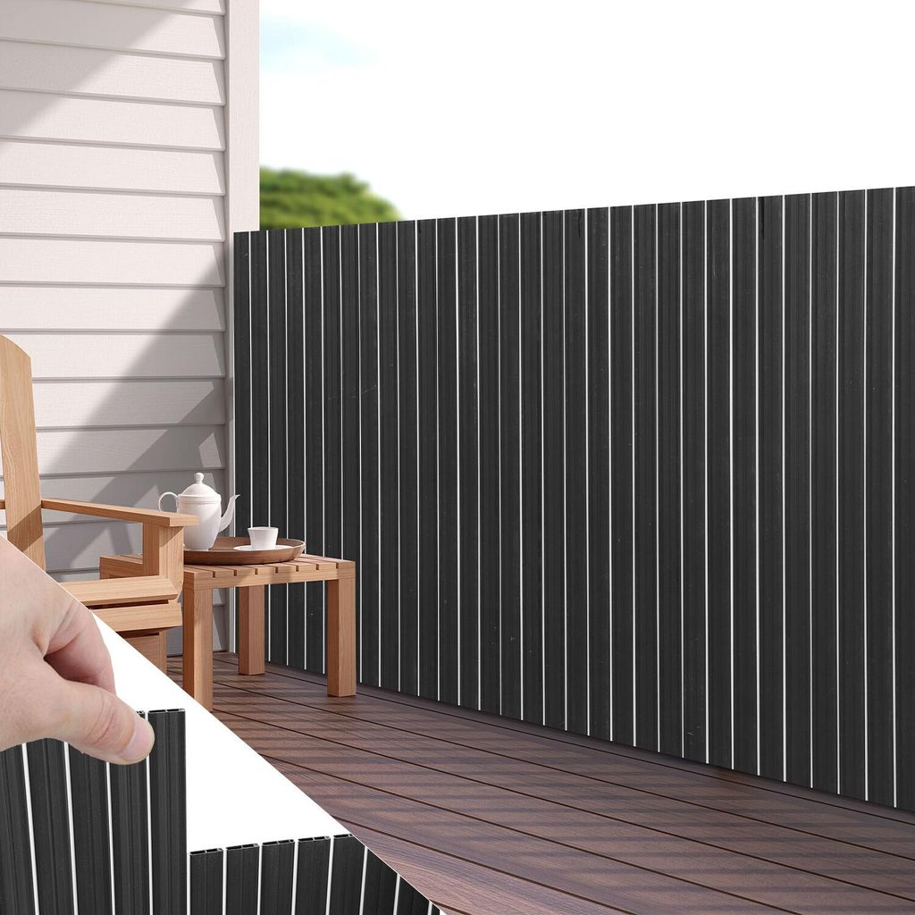A balcony with a wooden deck, a chair, a table with tea set, and a dark gray privacy screen.
