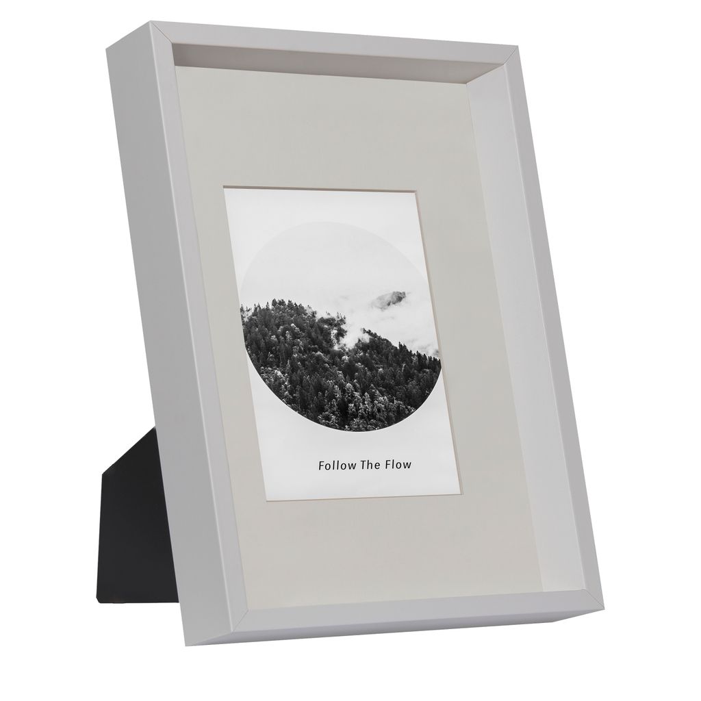 A white picture frame with a black stand, displaying a black and white photograph of a forest.