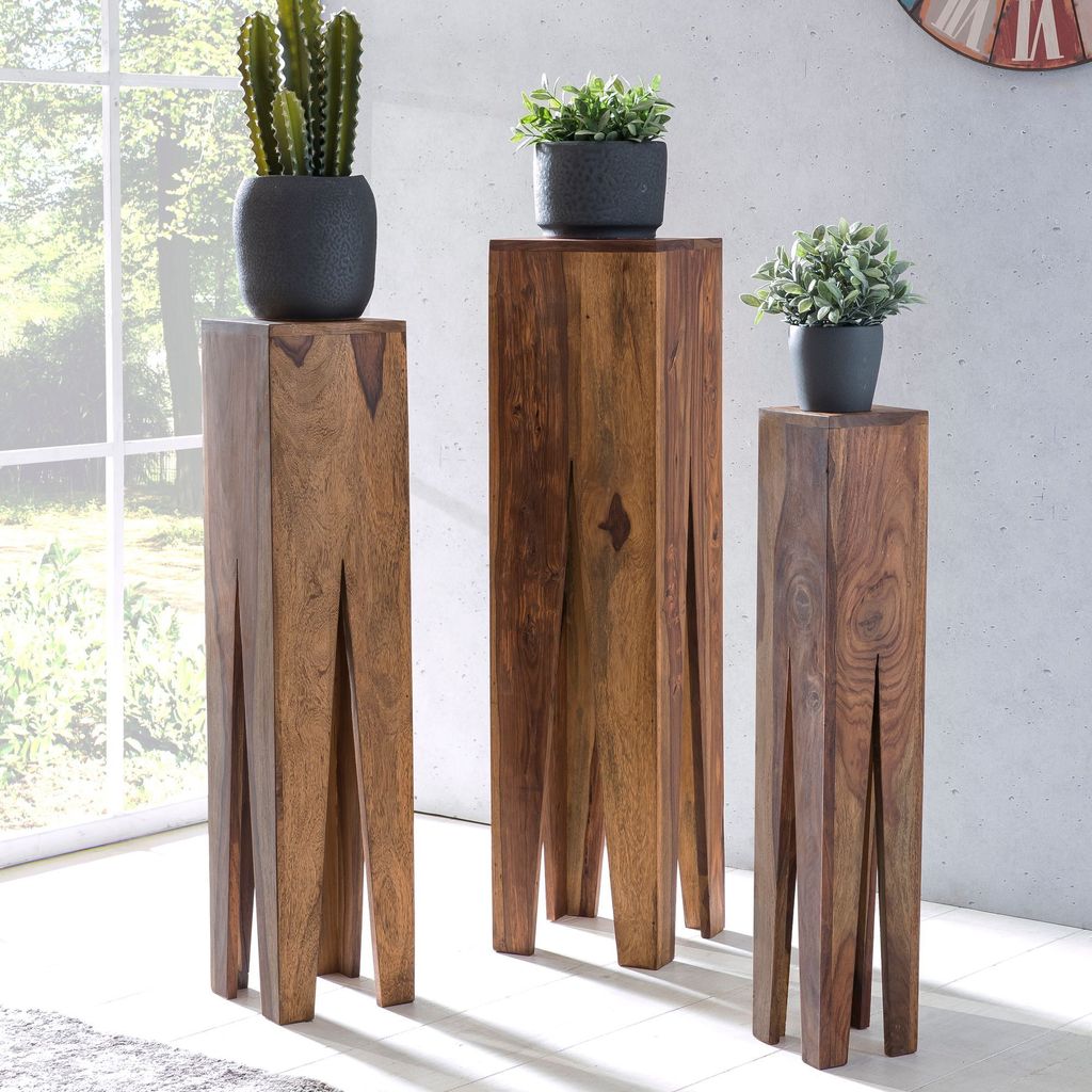 Three wooden plant stands of varying heights are placed in a room with a large window and light-colored walls.