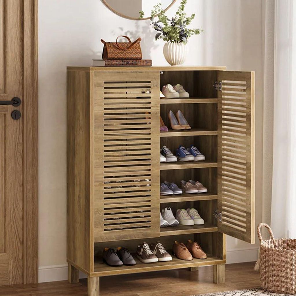 A wooden shoe cabinet with its door open, displaying shoes on shelves. A woven basket and a vase with flowers are on top of the cabinet.