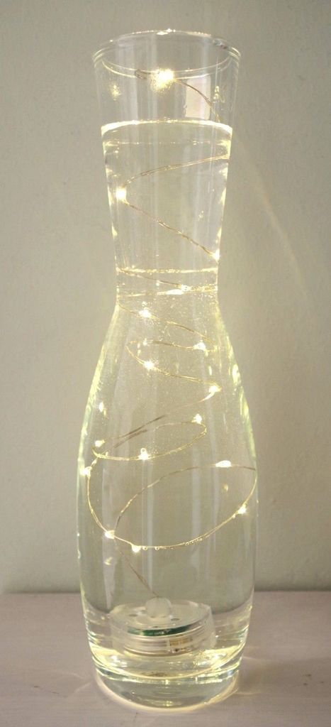 A clear glass vase filled with water and illuminated by a string of LED lights.