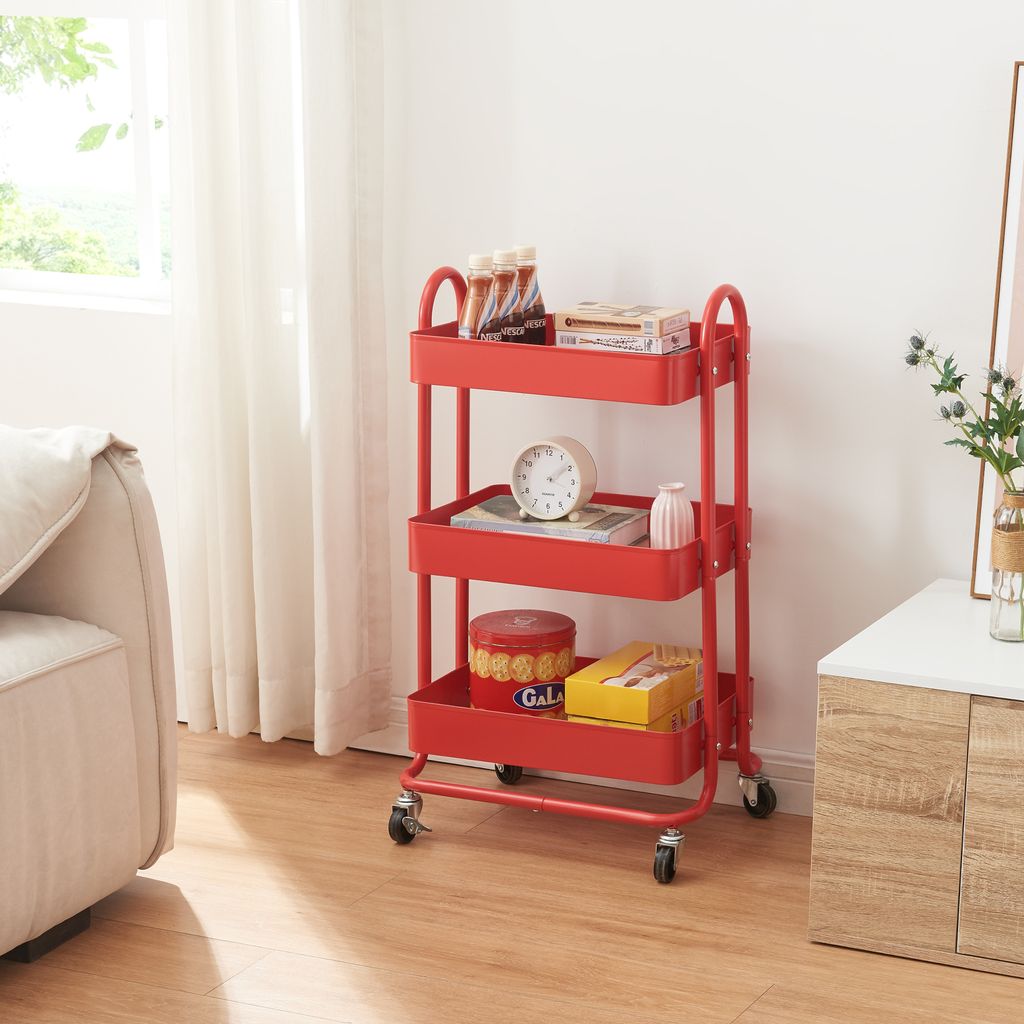A red three-tiered rolling cart filled with various items, placed next to a sofa and a cabinet.