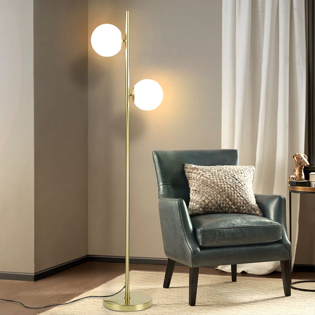 A modern floor lamp with two glass globes stands next to a dark green armchair with a textured cushion.