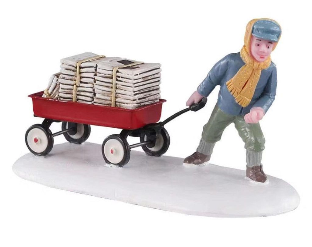 Miniaturfigur eines Jungen, der im Schnee einen roten Wagen zieht, der mit Zeitungen beladen ist.