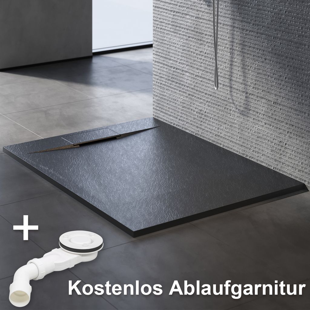 A black shower tray with a slate-like texture is shown on a tiled floor, with a white drain assembly in the foreground. Text indicates a free drain set.