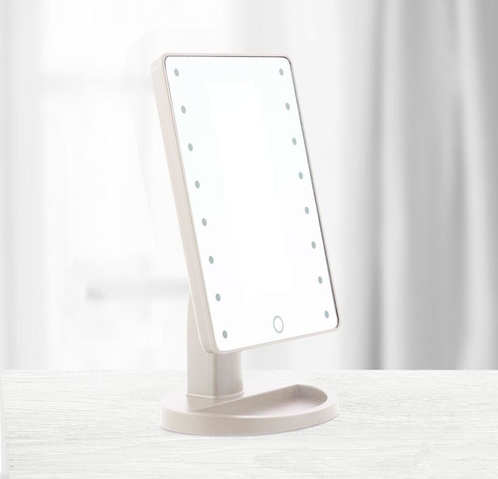 A makeup mirror with LED lights is placed on a white surface in front of a blurred background of white curtains.