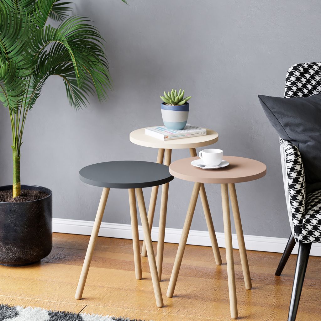 A set of three nesting side tables with a plant and a cup of coffee on them, next to a chair.