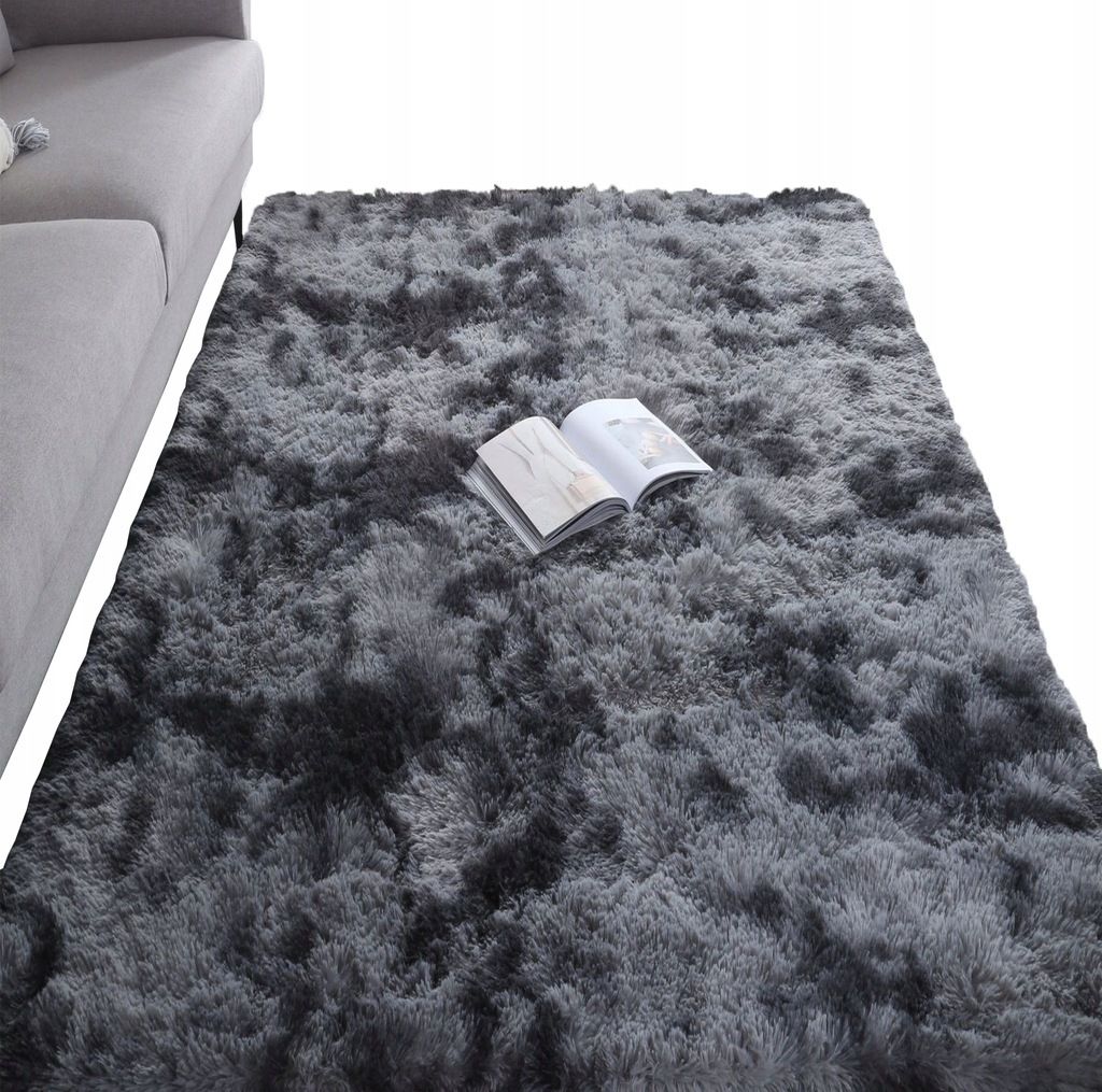 A dark gray shaggy rug is shown in a room, with a portion of a gray sofa visible on the left. An open book lies on the rug.