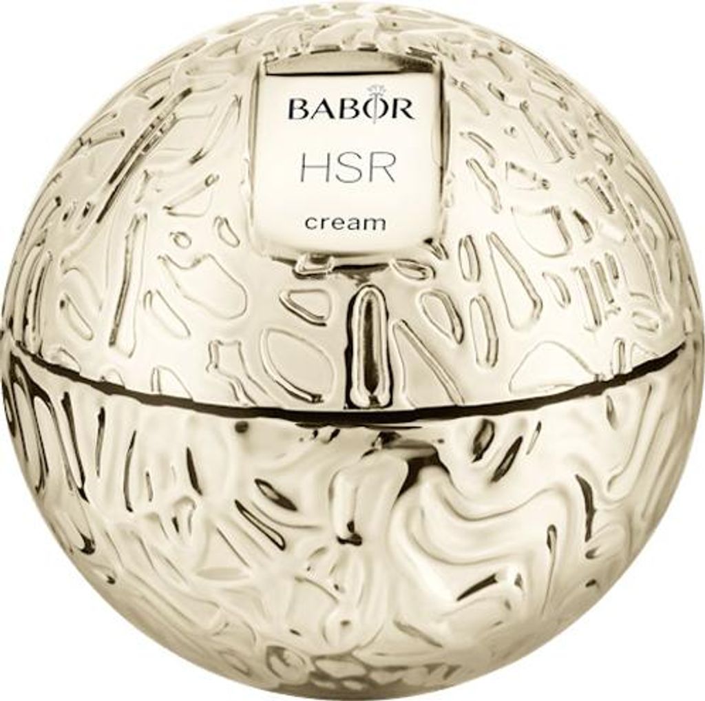 A close-up, studio shot of a round, gold-colored cosmetic jar with an ornate, textured surface and a white label.
