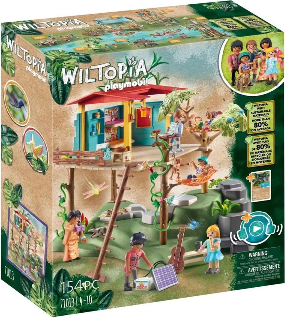 The image shows the packaging of a PLAYMOBIL Wiltopia Familienbaumhaus toy set, featuring the treehouse structure, figures, and accessories in a jungle-like environment.