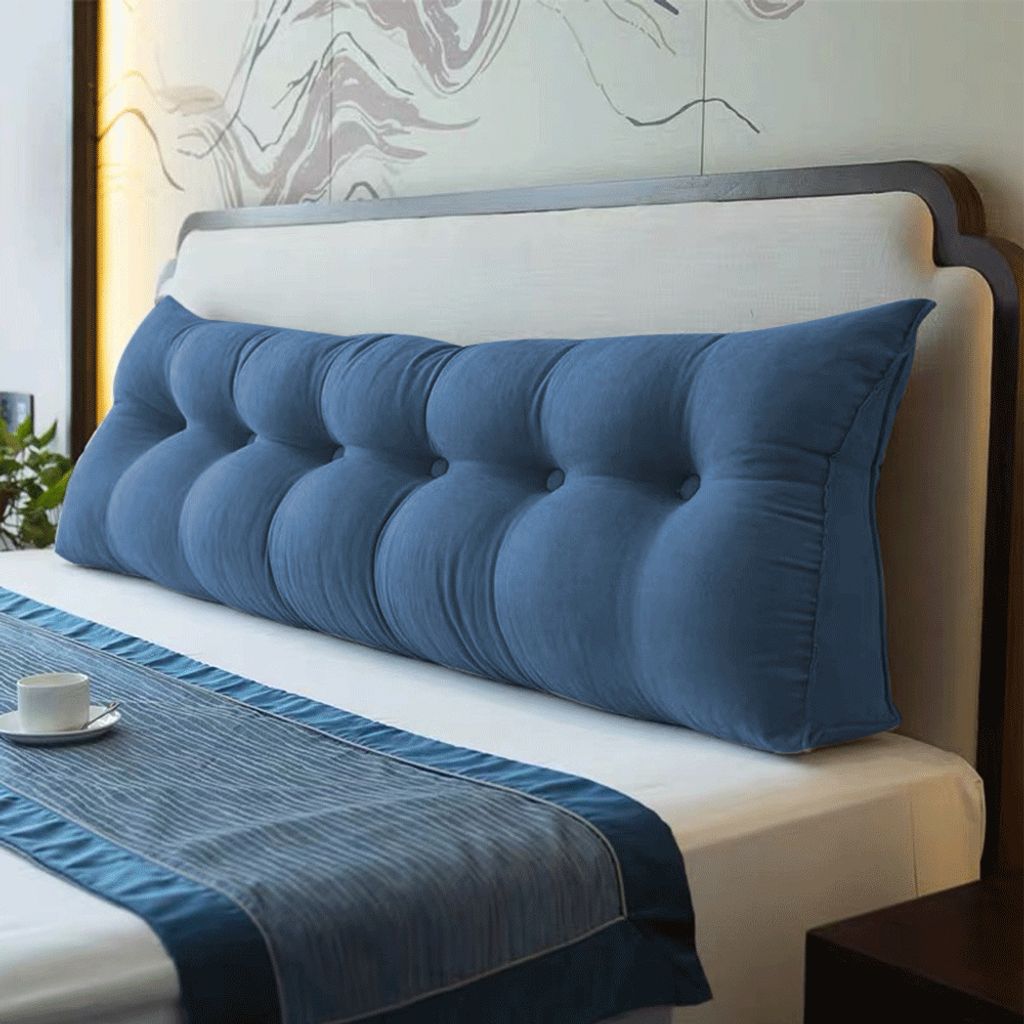 A dark blue wedge pillow is placed on a bed with a blue runner.