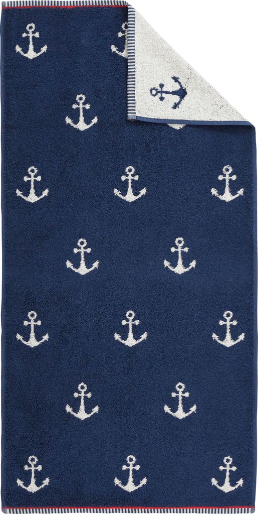 A folded navy blue towel with a pattern of white anchors, with a small section of the reverse side showing.