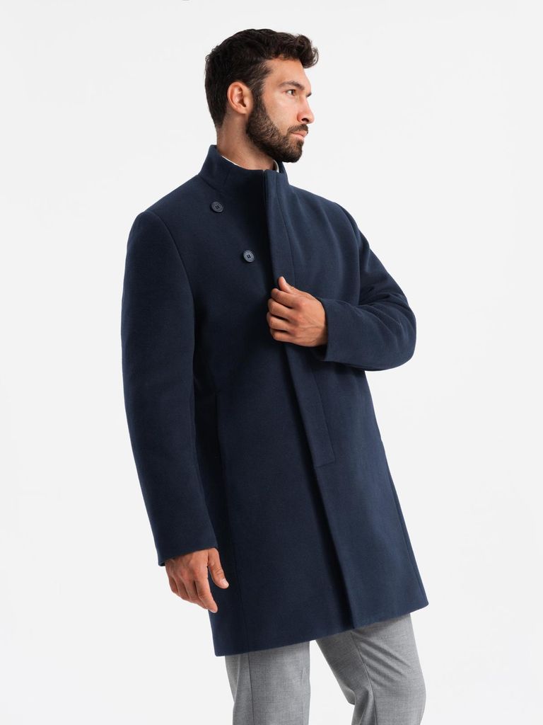 A man wearing a navy coat and grey pants, posing against a white background.