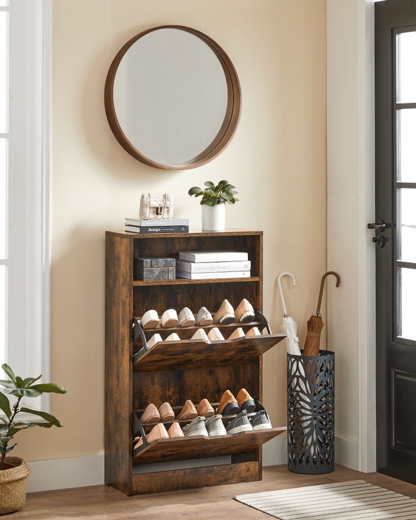 A narrow, dark wood shoe cabinet with two flip-down drawers is shown in a hallway. A round mirror hangs on the wall above the cabinet. An umbrella stand with two umbrellas sits to the right of the cabinet.