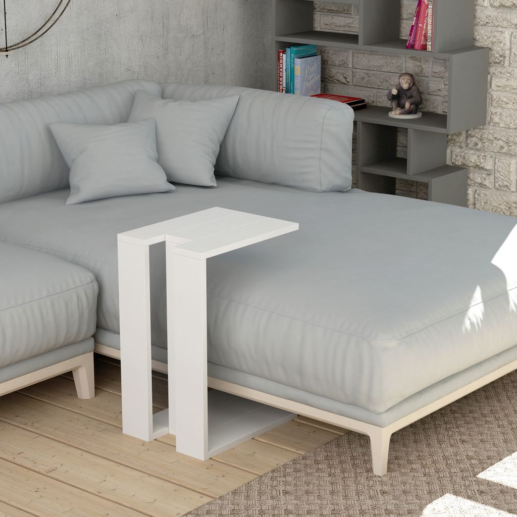 A white C-shaped side table is placed on a sectional sofa next to a bookshelf.