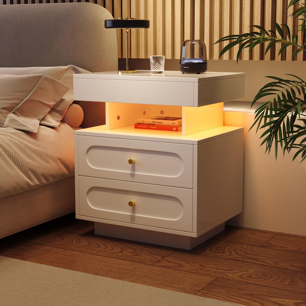 A modern white nightstand with two drawers and an open storage compartment with LED lighting, placed next to a bed in a bedroom setting.