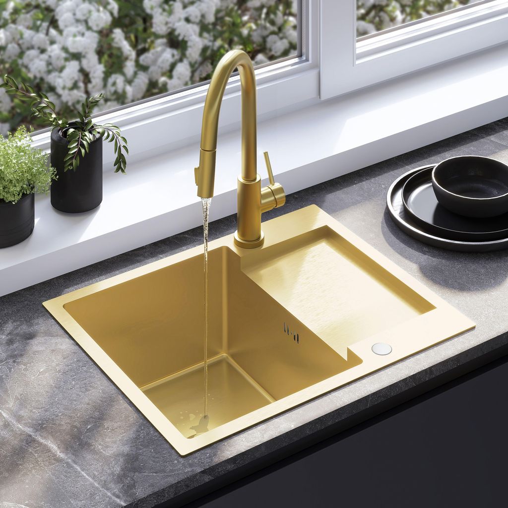 A gold sink with a faucet running water, set on a dark countertop with plants in the background and a window above.