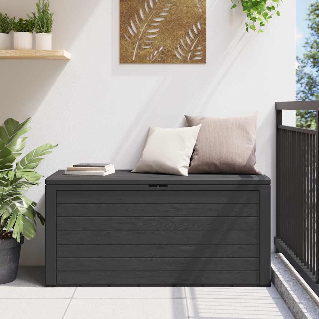 A dark gray storage box on a balcony with two pillows on top and a plant to the left.