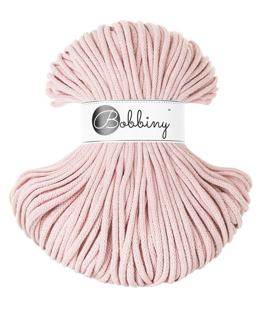 A spool of pastel pink macrame cord on a white background.