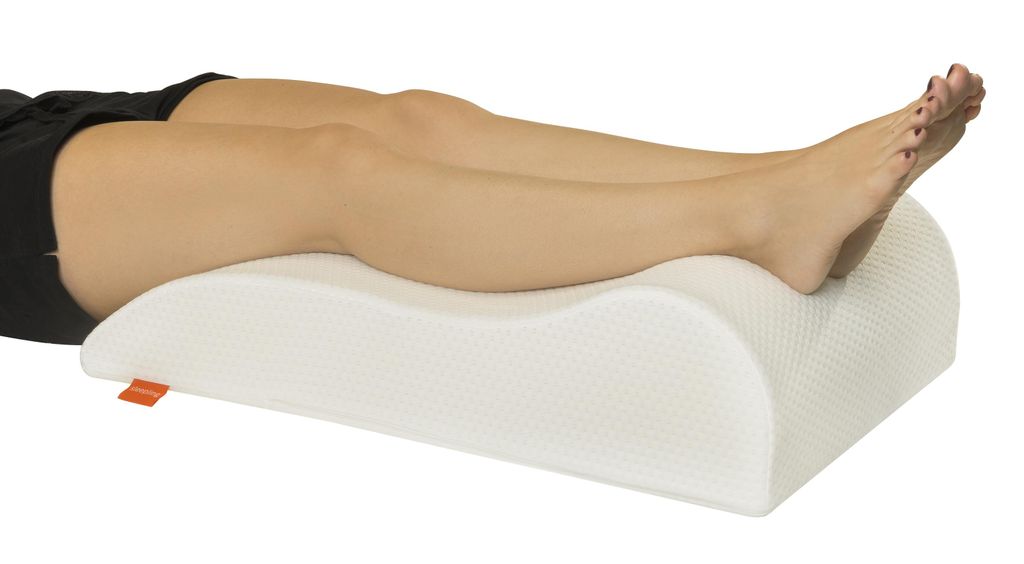 A person's legs are resting on a white leg elevation pillow.