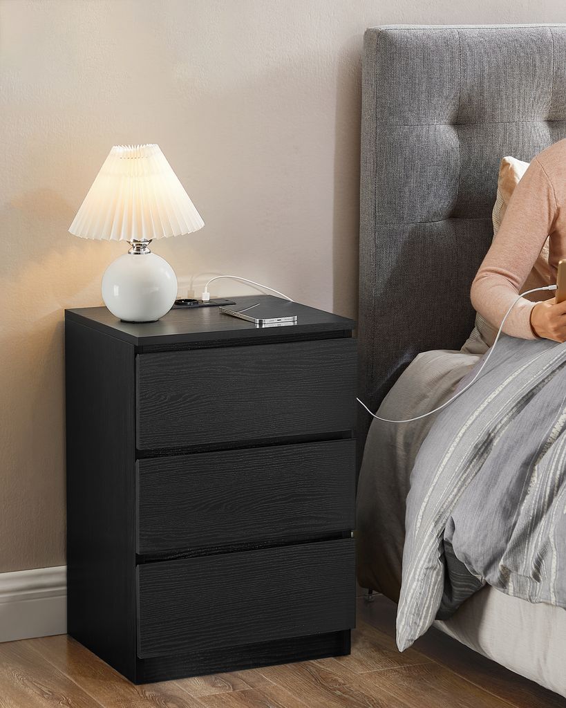 A person is in bed next to a nightstand with a lamp and a phone.