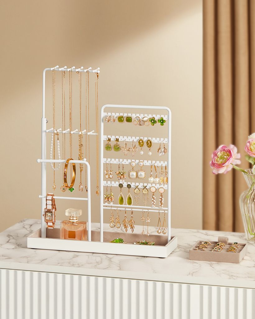 A white jewelry organizer stand filled with various necklaces, earrings, a watch, and a perfume bottle, placed on a marble-like surface.