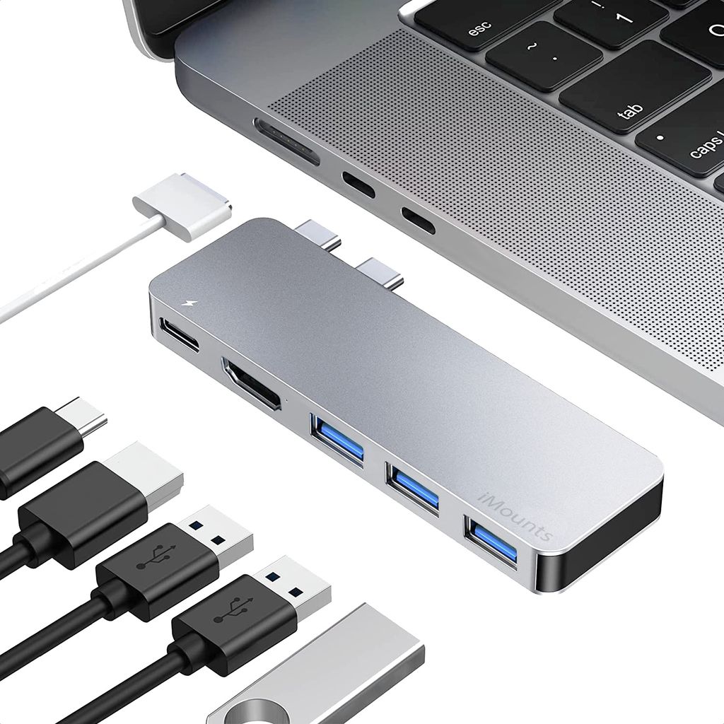 A silver USB-C hub is shown connected to a silver laptop, with various cables and a USB drive nearby.