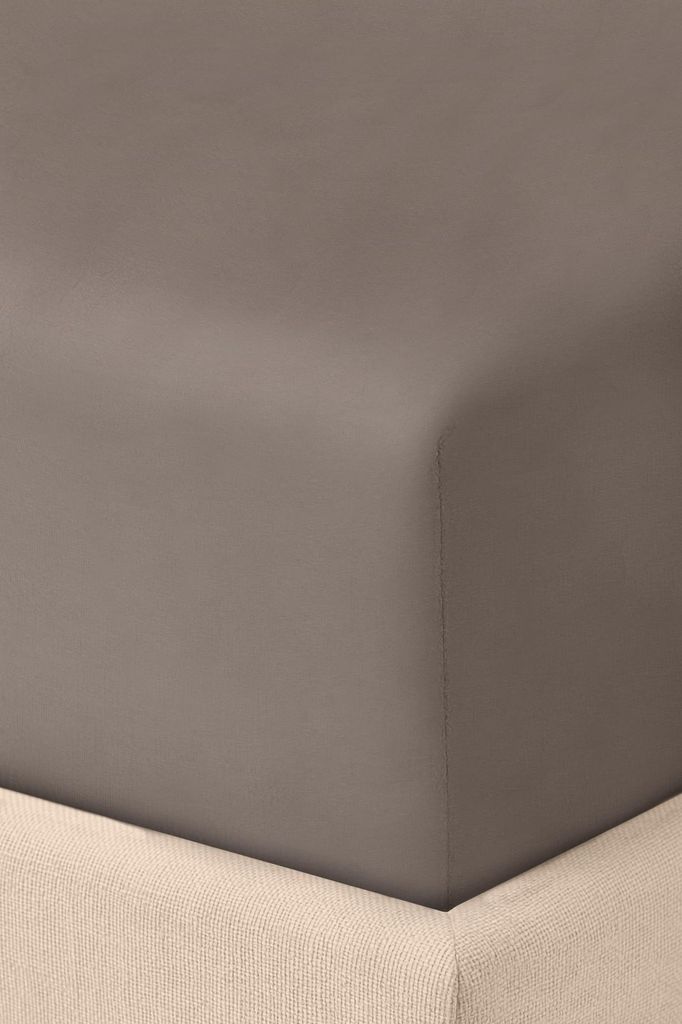 A close-up view of a fitted sheet on a bed, showing the corner and the texture of the fabric.