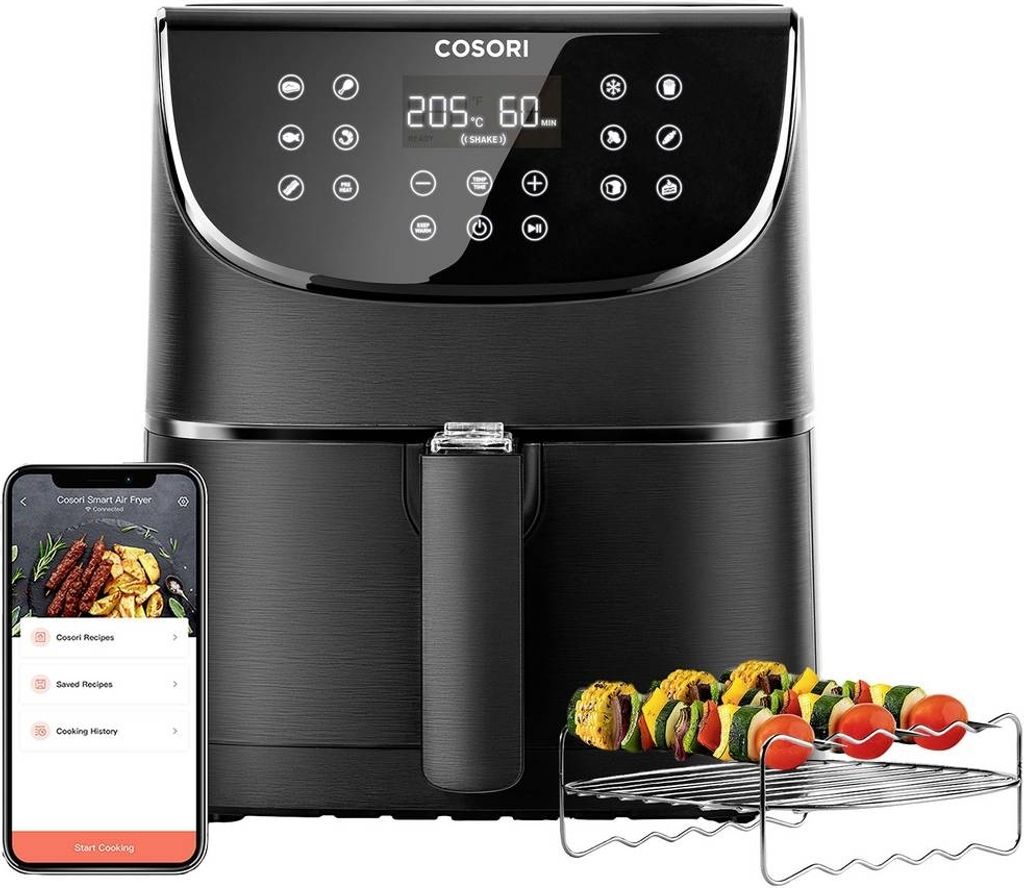 A black air fryer with a smartphone displaying recipes next to it, and a rack of food skewers in front.