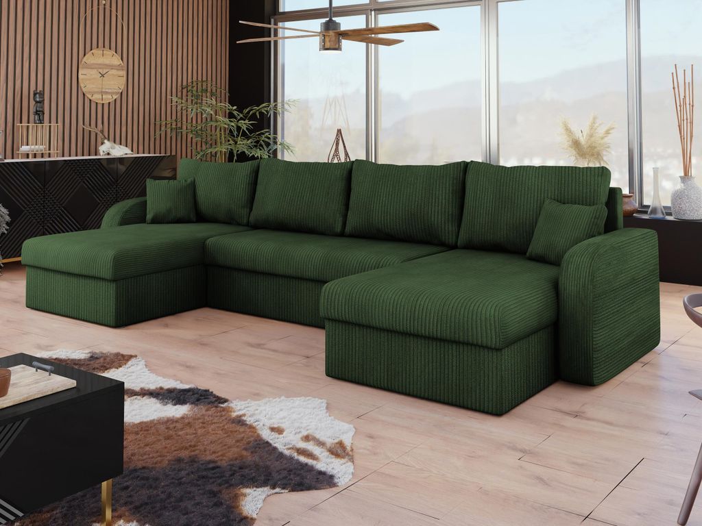 A spacious living room with a large green sectional sofa, a cowhide rug, and a black coffee table, featuring a large window with a view of mountains.