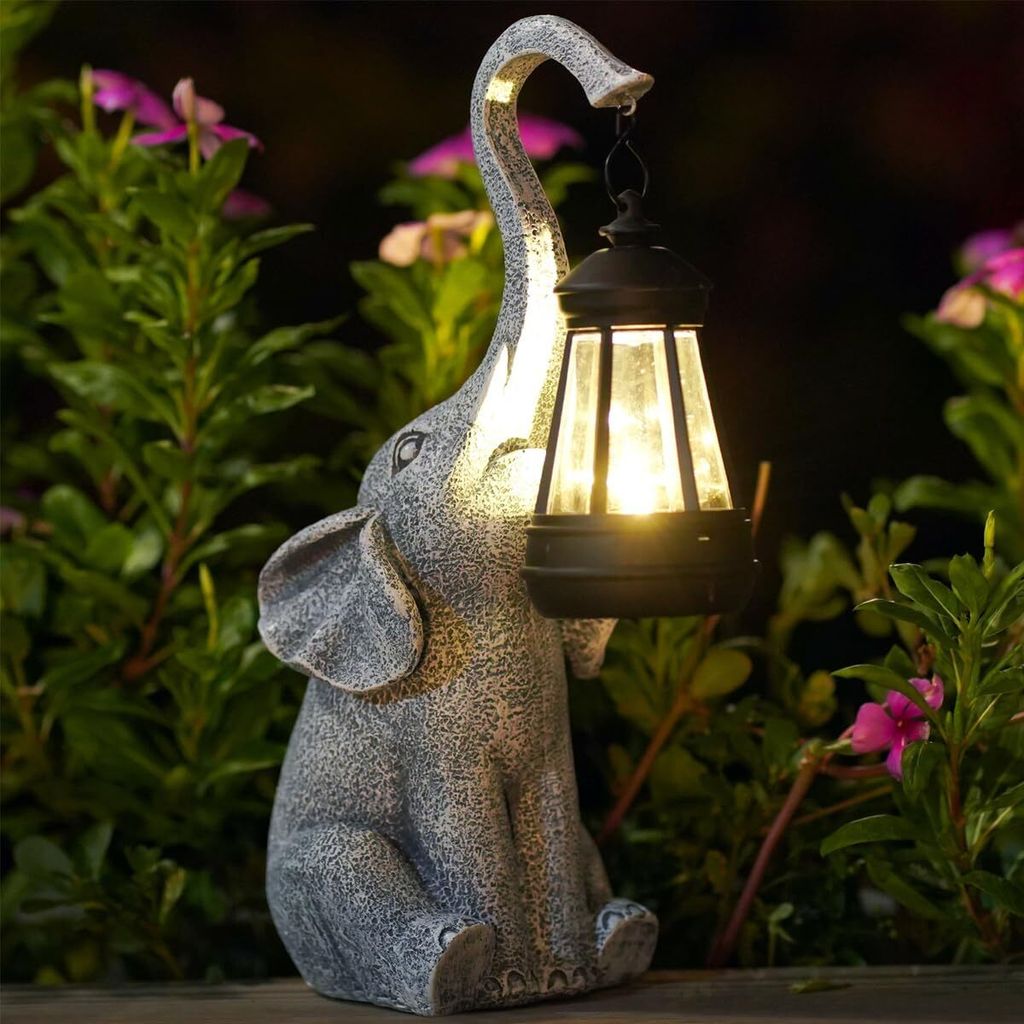 A solar-powered elephant statue holding a lantern in a garden setting at dusk.