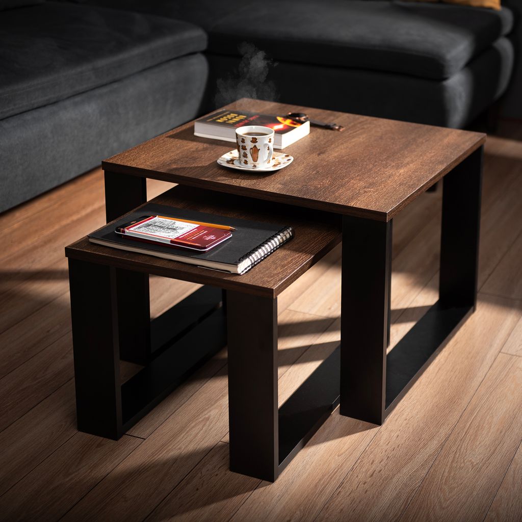 A set of nesting coffee tables in a living room setting, with a book, coffee cup, and cigarette on the top table.