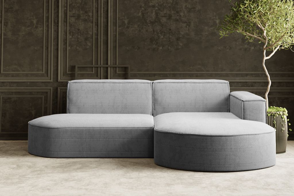 A modern, modular sectional sofa with rounded edges upholstered in corduroy fabric, set against a dark paneled wall with a potted plant and tree.