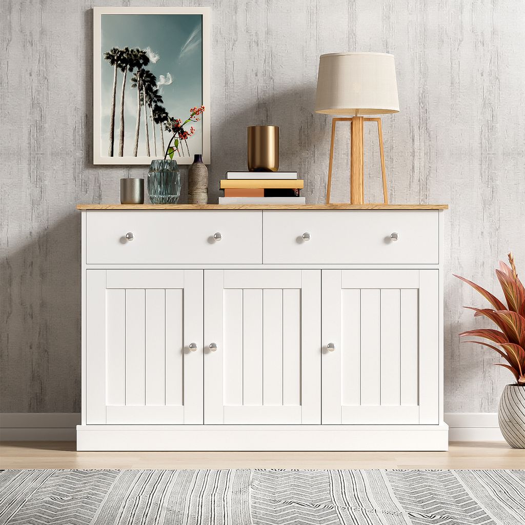 A white sideboard with wooden top, decorated with a framed picture, books, and a lamp.