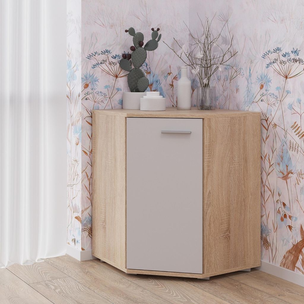 A corner cabinet with a light wood finish and a white door, decorated with a cactus and branches on top. It is placed in a room with floral wallpaper and a white curtain.