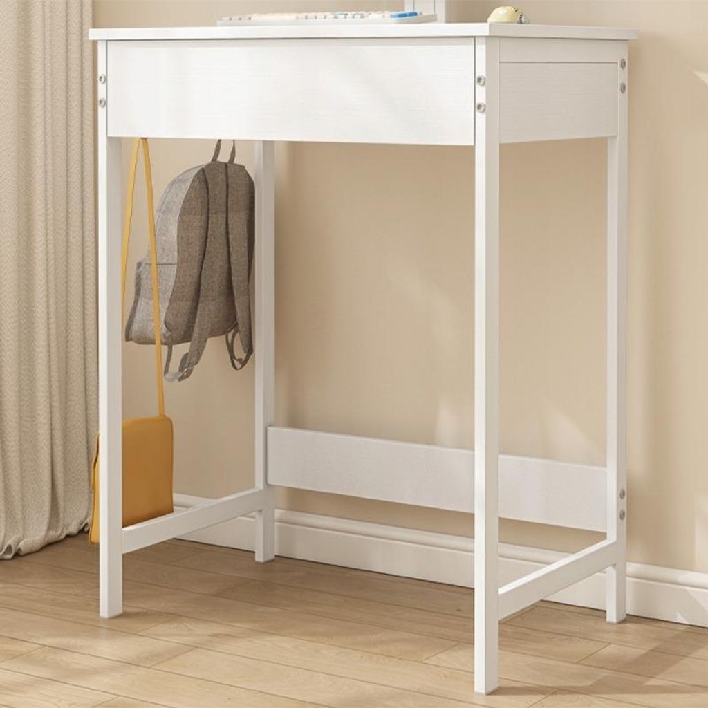 A white desk with a backpack and purse hanging on it, set against a light beige wall and wooden floor.