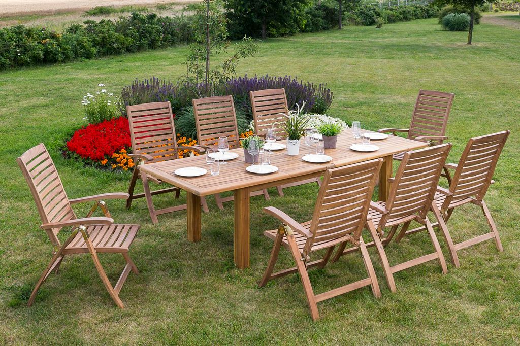 A wooden garden dining set with a table and chairs set up on a lawn, surrounded by flowers and greenery.