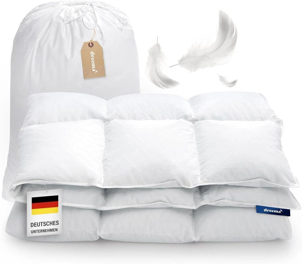 A white down comforter is folded and displayed with a storage bag and feathers in the background.
