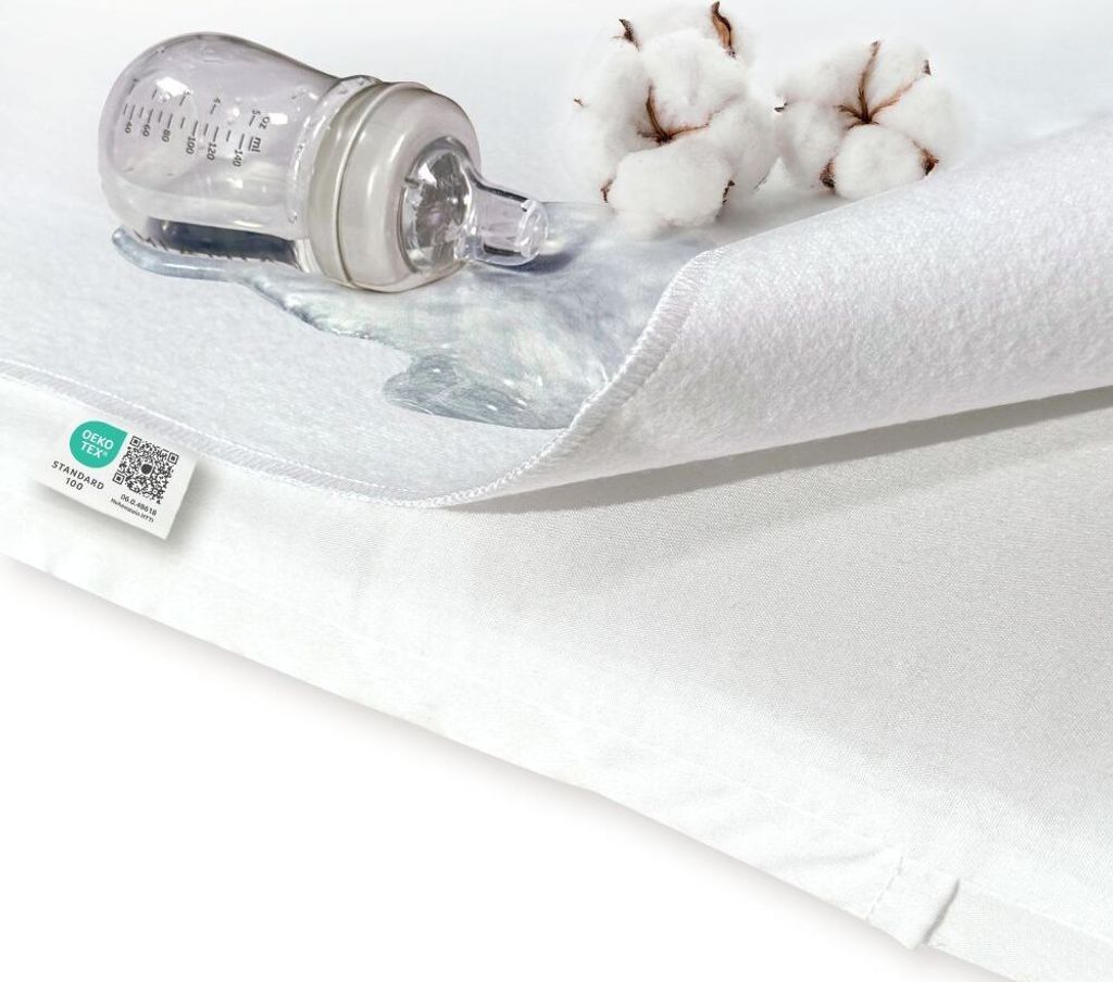 A close-up of a white waterproof mattress protector with a baby bottle and spilled liquid on it, along with cotton balls.