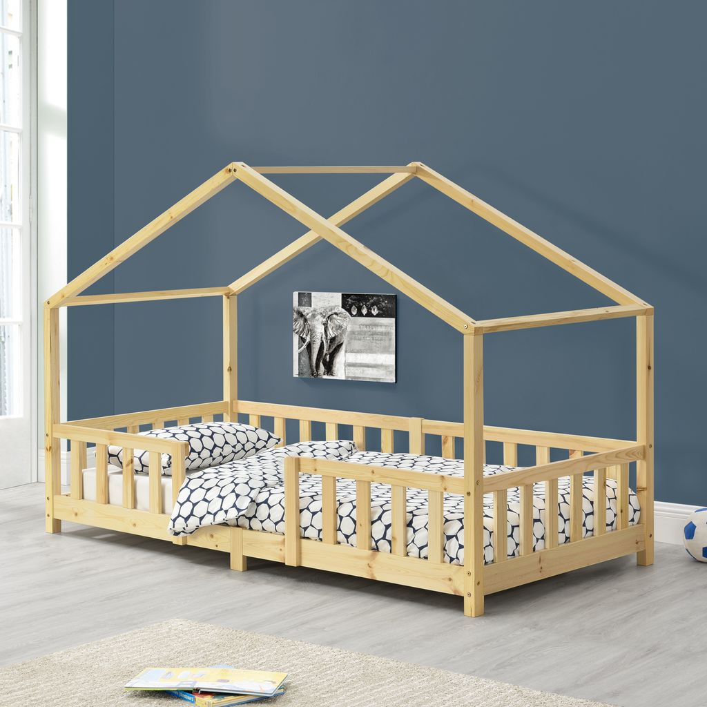 A wooden house-shaped bed frame with a mattress and bedding, set against a blue wall.