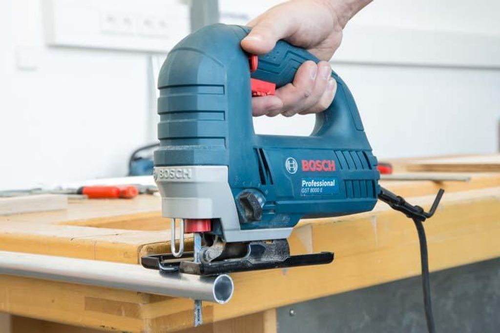 A hand holding a Bosch jigsaw over a piece of wood.