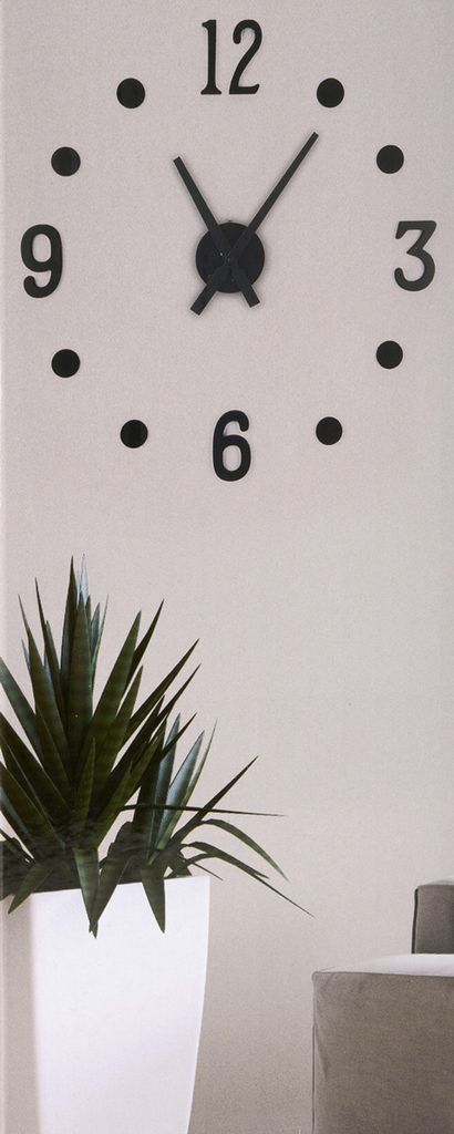 A wall clock with black hands and numbers on a white background, with a potted plant in the foreground.
