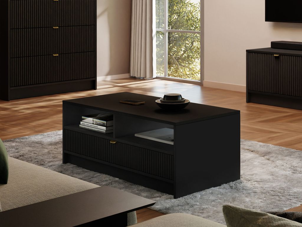 A modern living room with a black coffee table in the foreground, placed on a gray rug. A large window with curtains is visible in the background, letting in natural light.