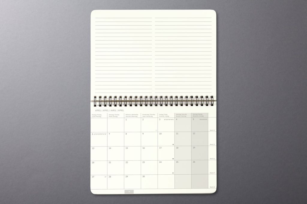 An open desk calendar with a monthly planner and lined note pages, laid flat on a gray surface.