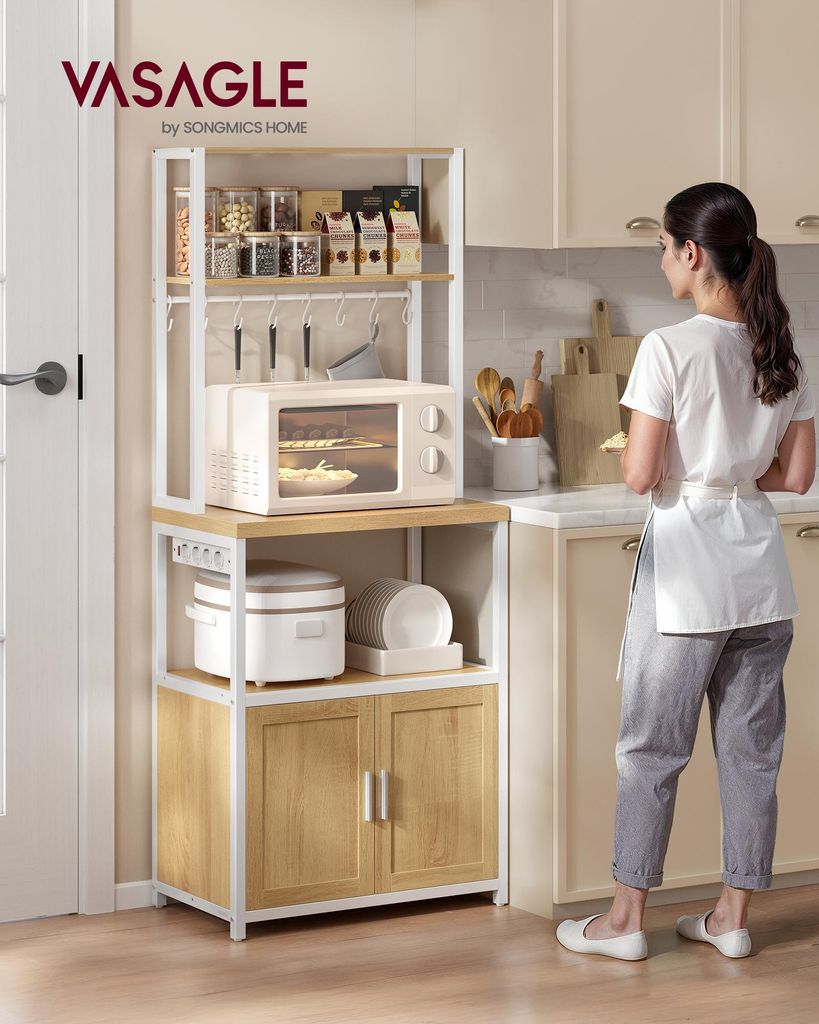 A woman is standing next to a kitchen baker's rack filled with kitchen appliances and pantry items.