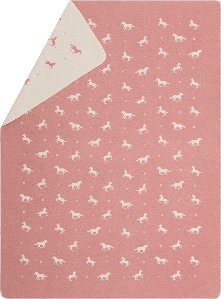 A flat lay of a pink blanket with a repeating pattern of white horses and small dots. The blanket is folded diagonally, showing two sides with slightly different patterns.