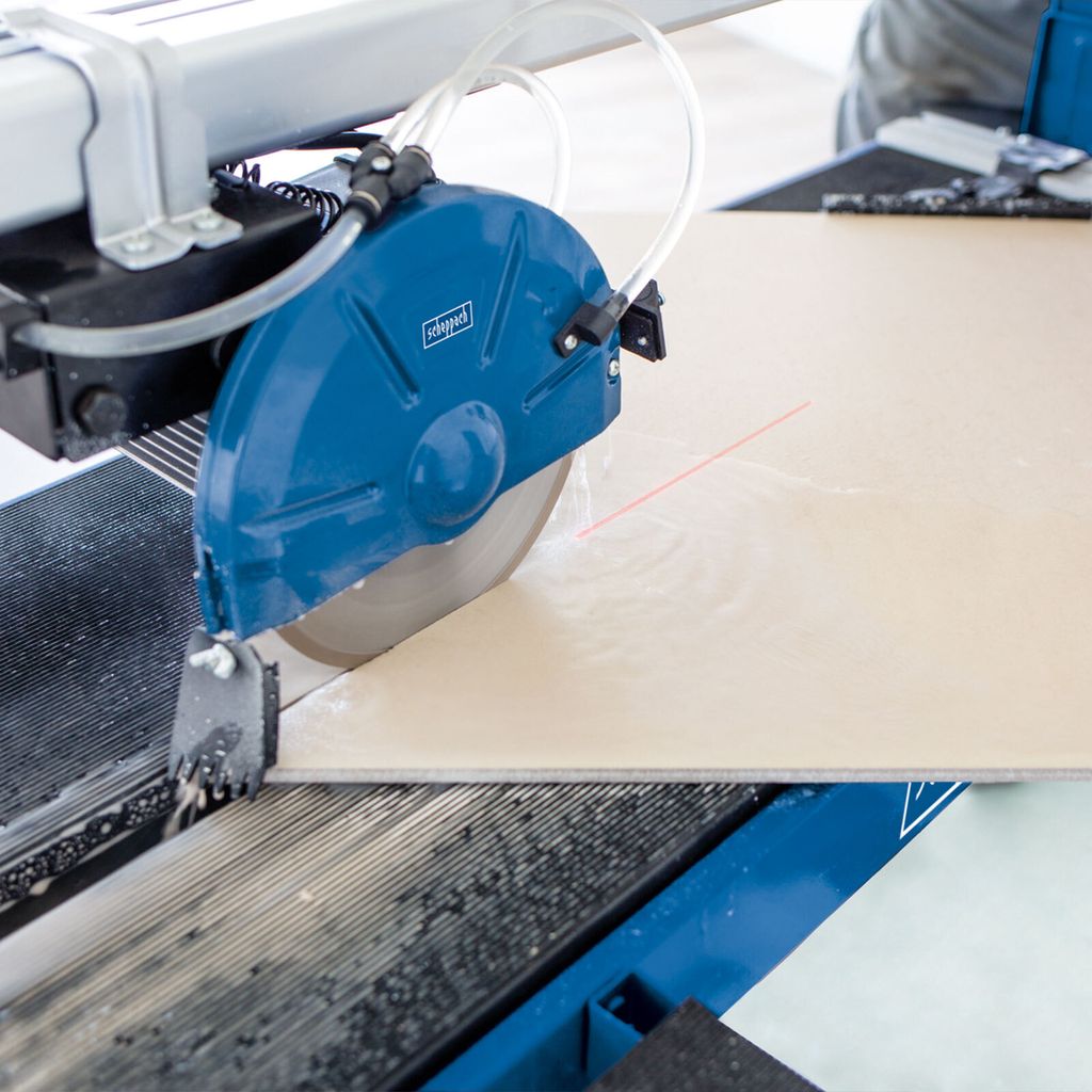 A close-up of a tile saw cutting a beige tile.