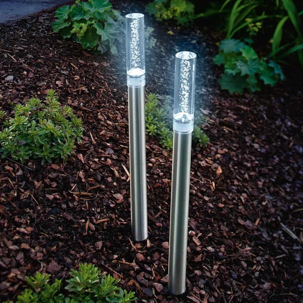 Two solar-powered garden lights with bubble effects are shown in a garden bed with mulch and plants.