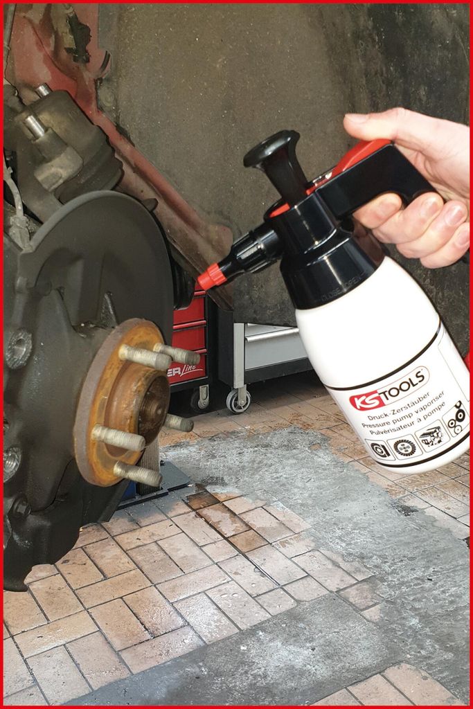 A hand is holding a spray bottle near a car's brake assembly.