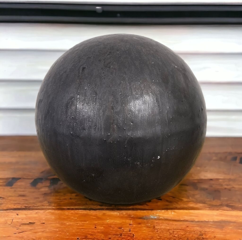 A dark, spherical object sits on a wooden surface in front of a slatted background.